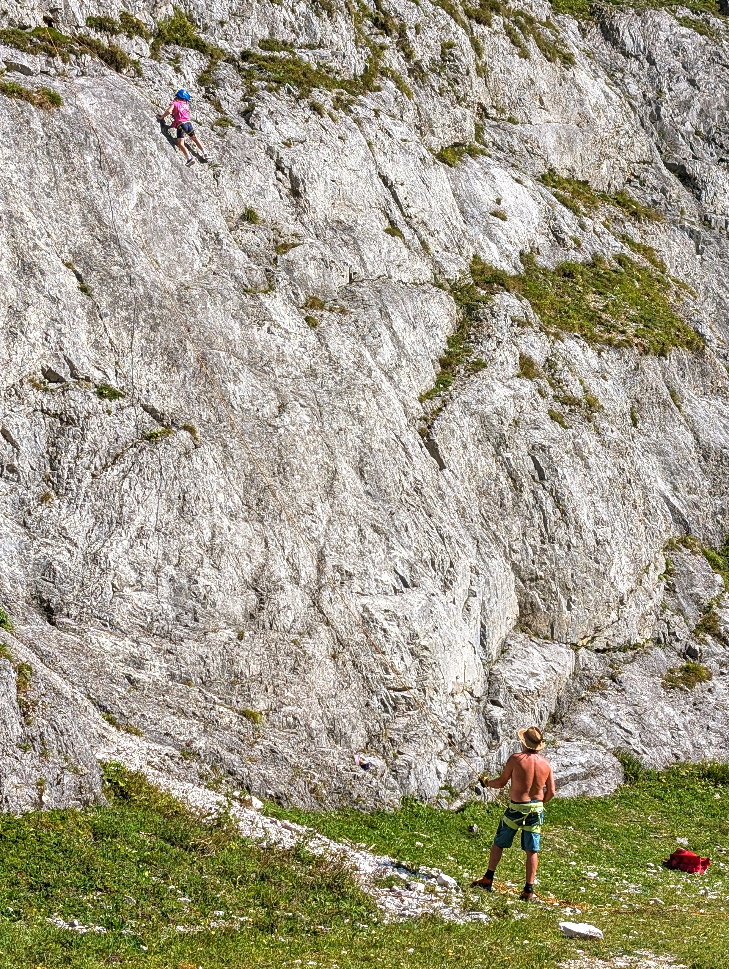 Ein Kind klettert eine Felswand hinauf, unten sichert ein Erwachsener